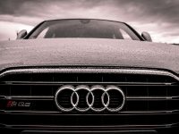 Close-up of a rain-covered Audi car grille showcasing luxury and elegance under cloudy skies.